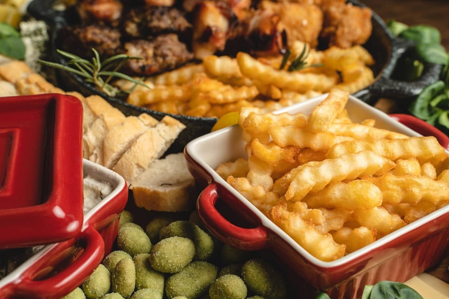 Roštilj u tiganju sa pomfritom, hlebom i prilozima u crvenim posudama