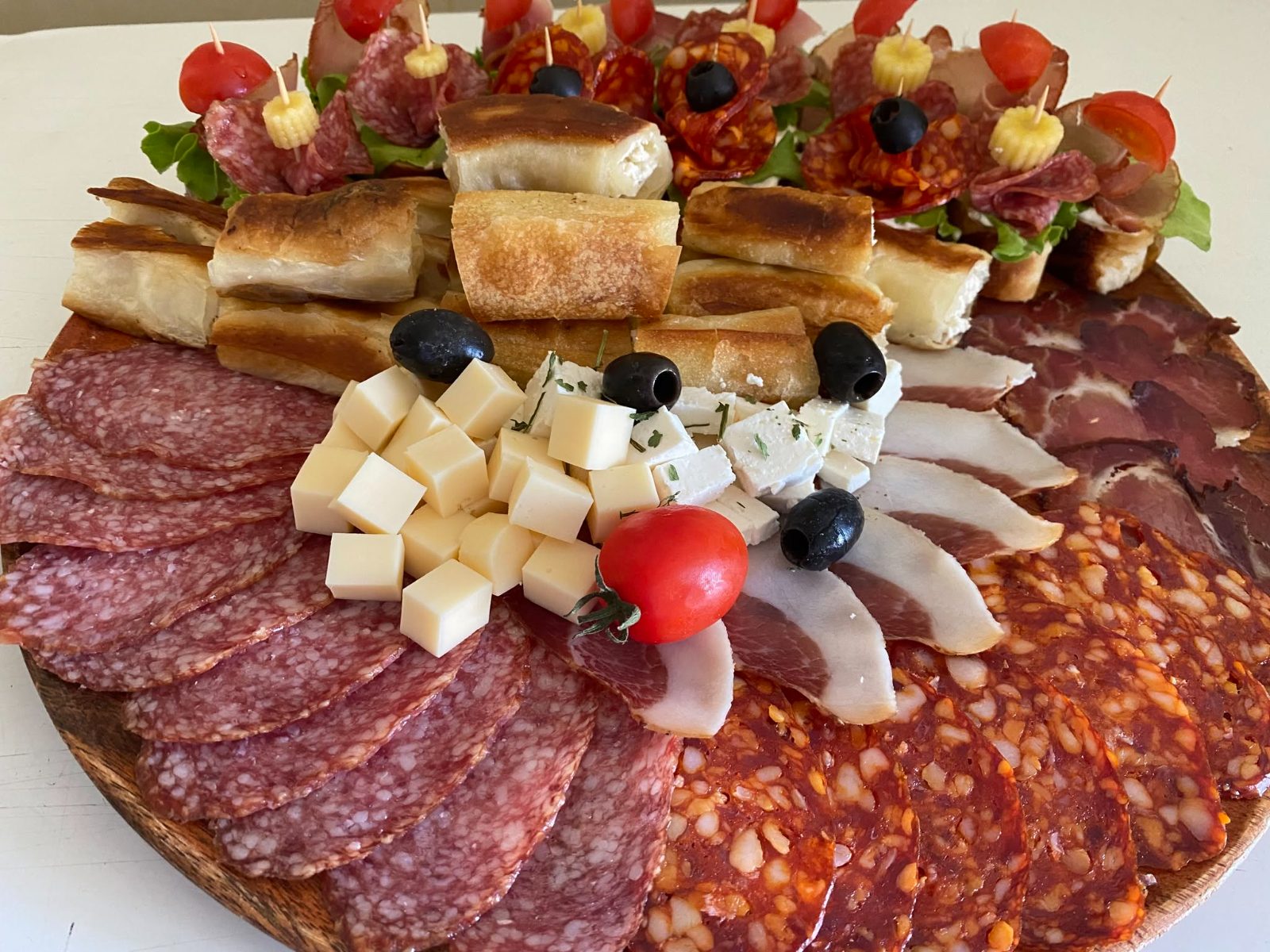 Veliki plato suhomesnatog i sireva sa komadima pite i peciva, uz ražnjiće u pozadini
