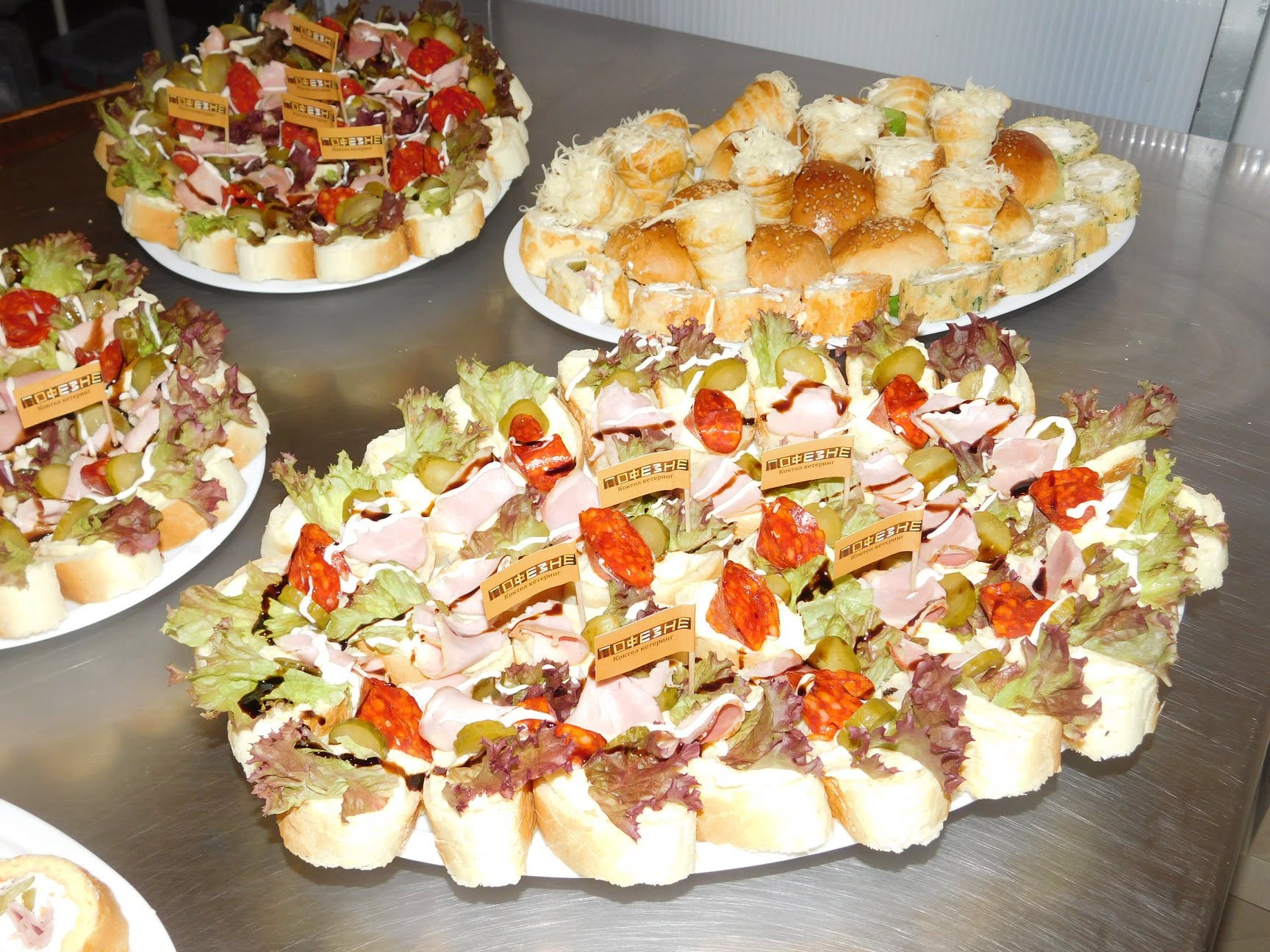 Platoi kanapea sa šunkom, kulenom i zelenom salatom, uz plato slanih peciva