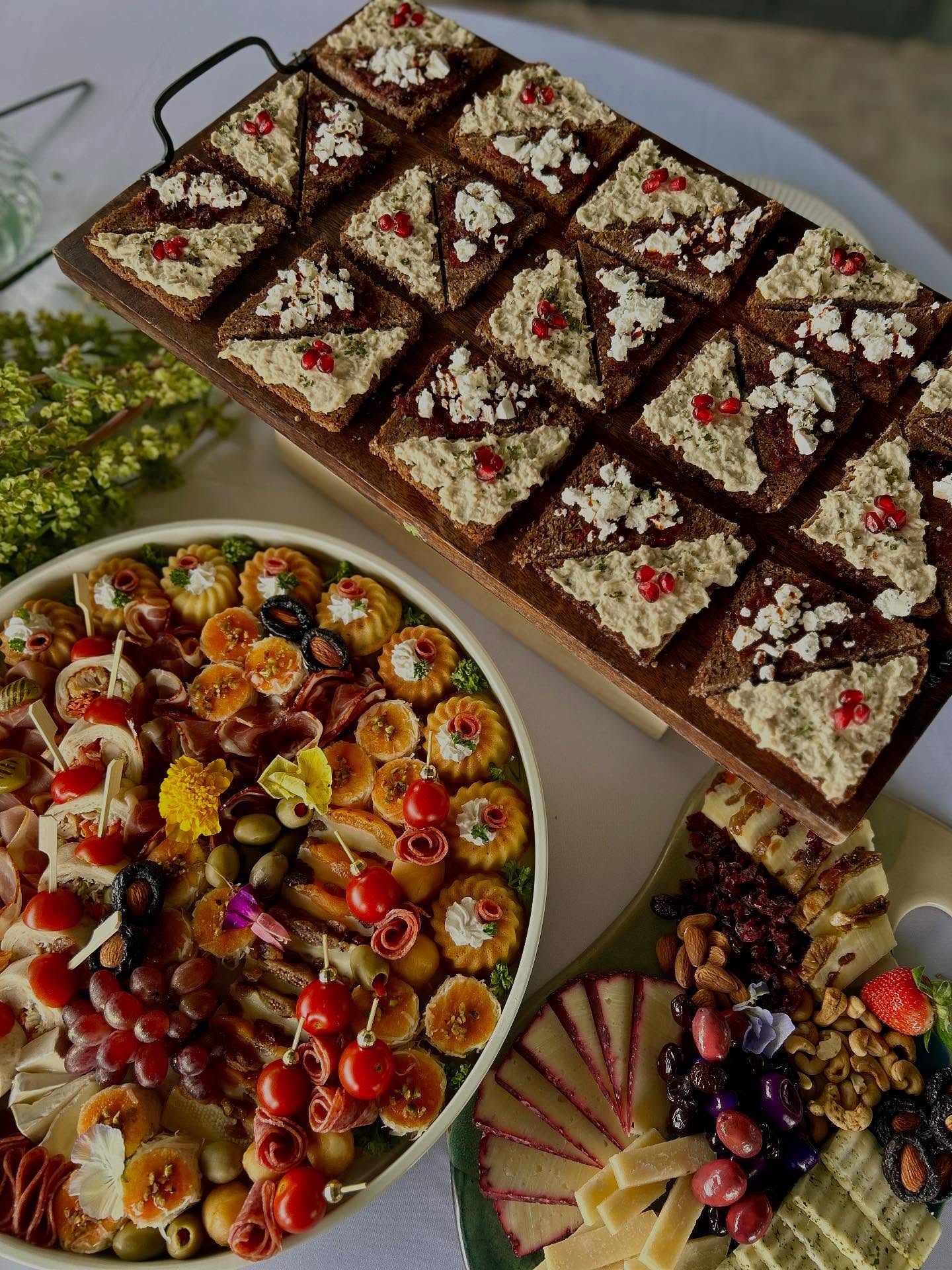 Drvena daska sa kanapeima na raženom hlebu, uz veliki okrugli plato zalogaja