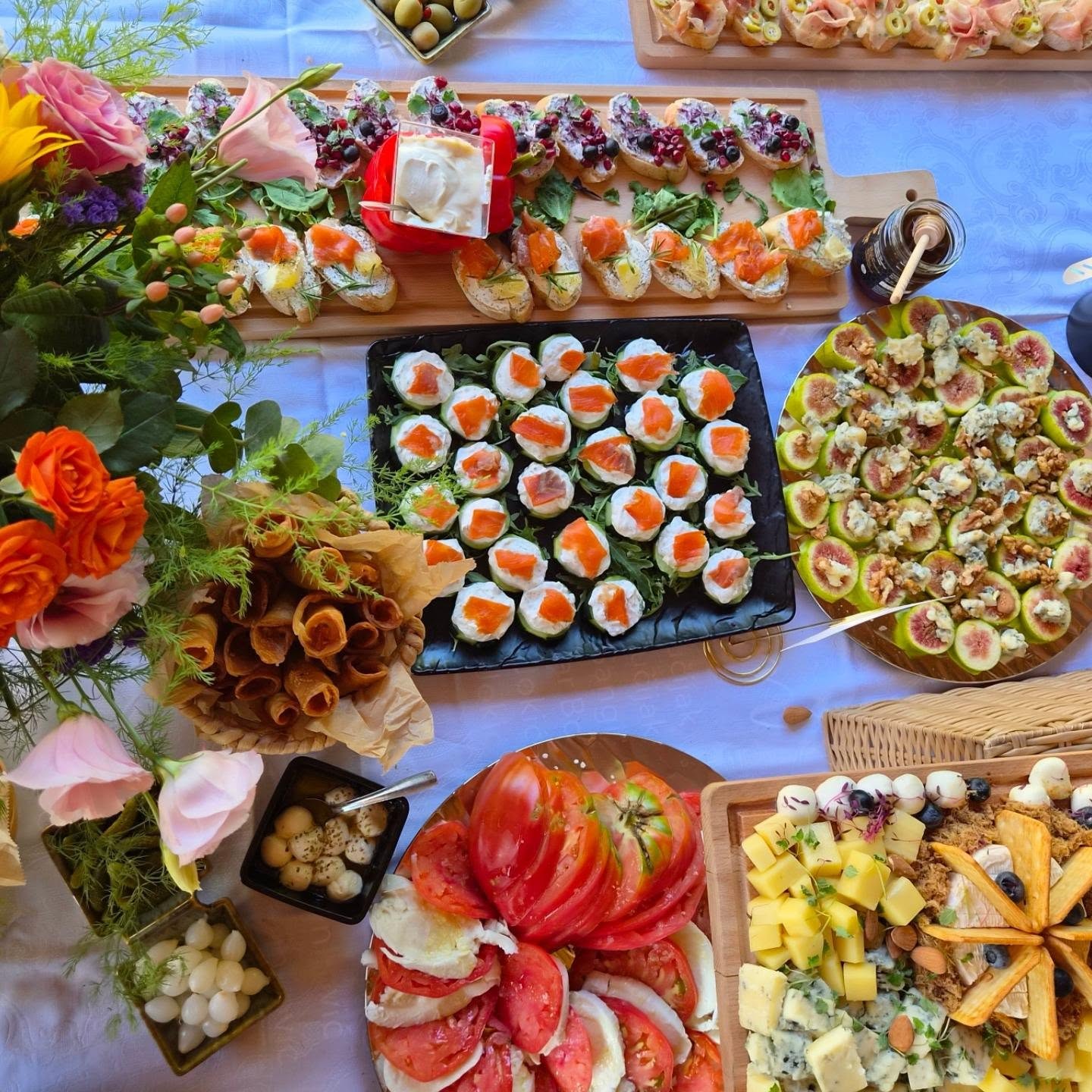 Sto sa cvećem snimljen odozgo — kanapei sa dimljenim lososom, bruskete sa bobičastim voćem, smokve sa gorgonzolom i karpačo od paradajza — Umami Ketering