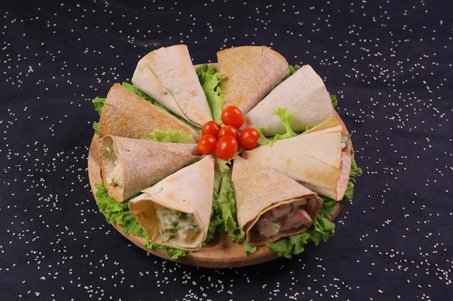 Tortilja rolnice na drvenoj dasci, sa zelenom salatom i čeri paradajzom