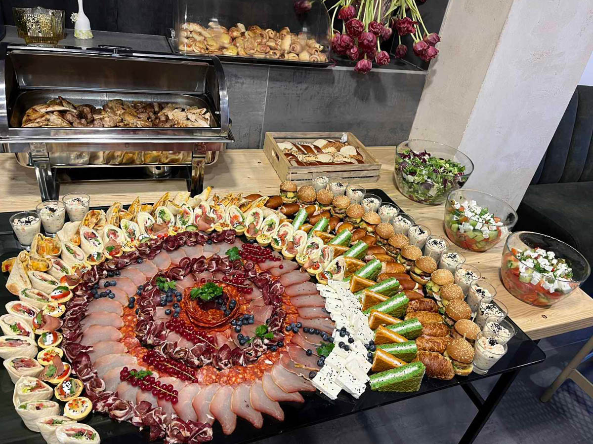 Veliki ovalni plato suhomesnatog sa rolnicama i mini burgerima, uz grejač i salate u bokalima